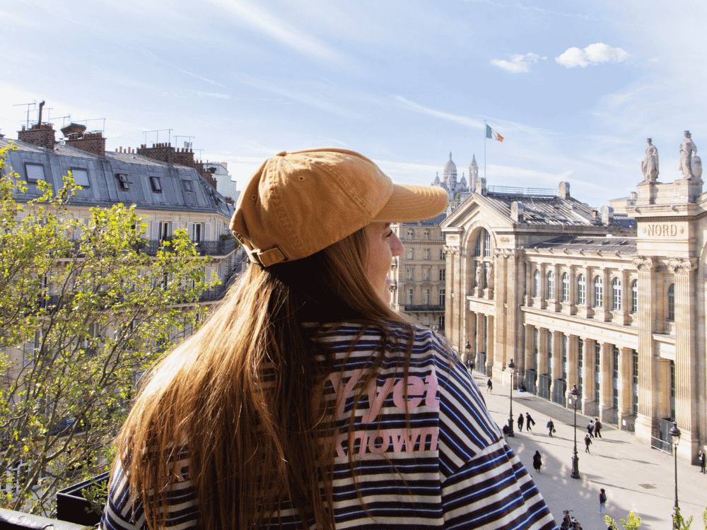 A woman wearing a stylish hat, smiling while standing outdoors in a sunny environment.
