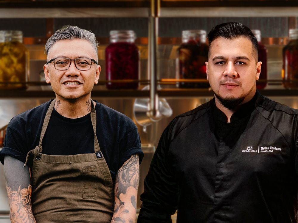 Two chefs in white uniforms stand side by side in a professional kitchen, smiling and ready to cook.
