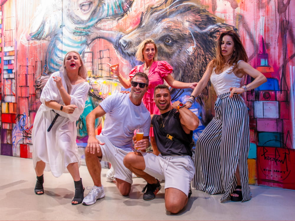A diverse group of individuals smiling and posing in front of a colorful mural.