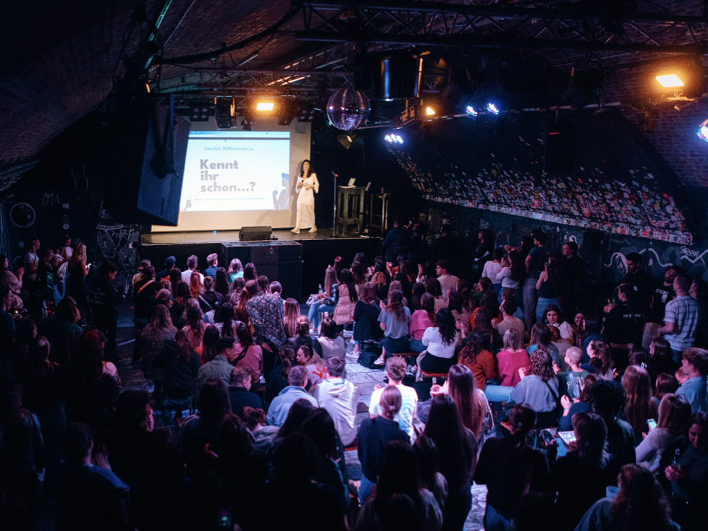 A large crowd of people gathered in a dimly lit room, creating a lively and energetic atmosphere.