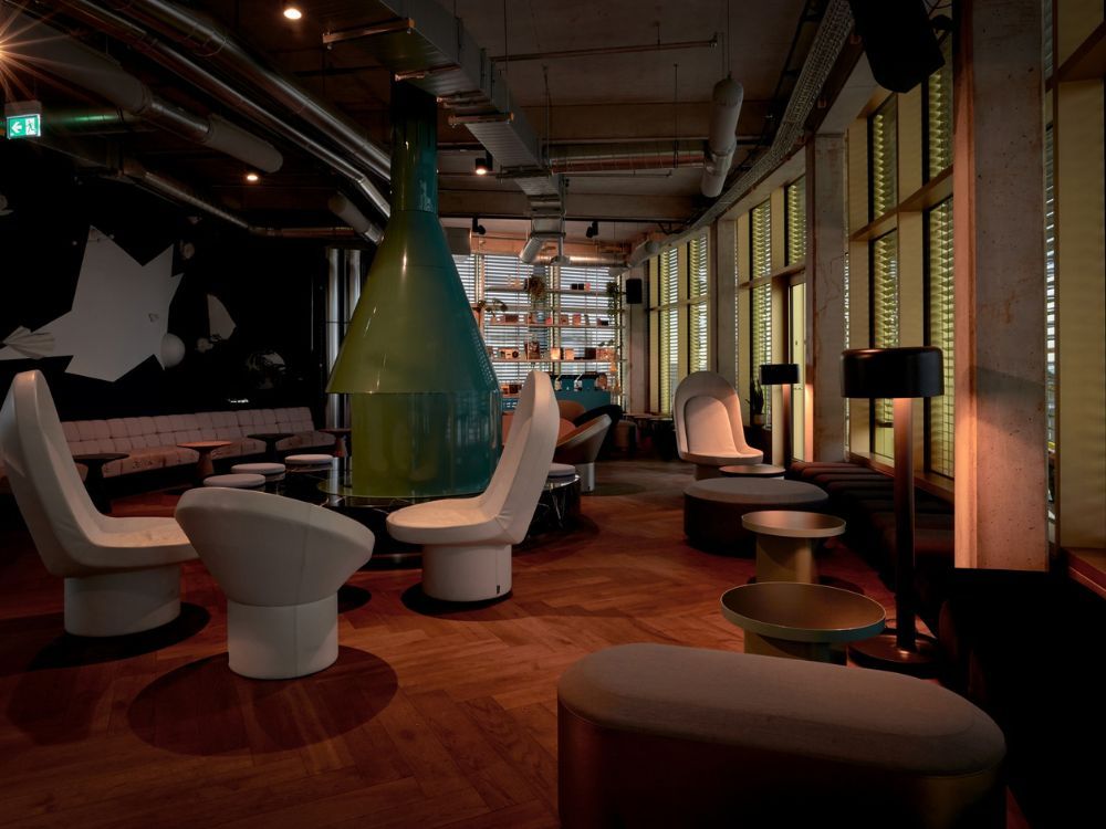 Spacious hotel bar and lounge with warm lighting, a cosy fireplace, parquet flooring, and a long pink banquette sofa.