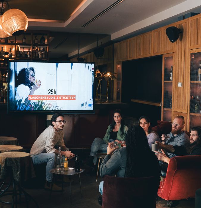 Group of professionals attending a creative workshop presentation in a modern hotel lounge with a large display screen.