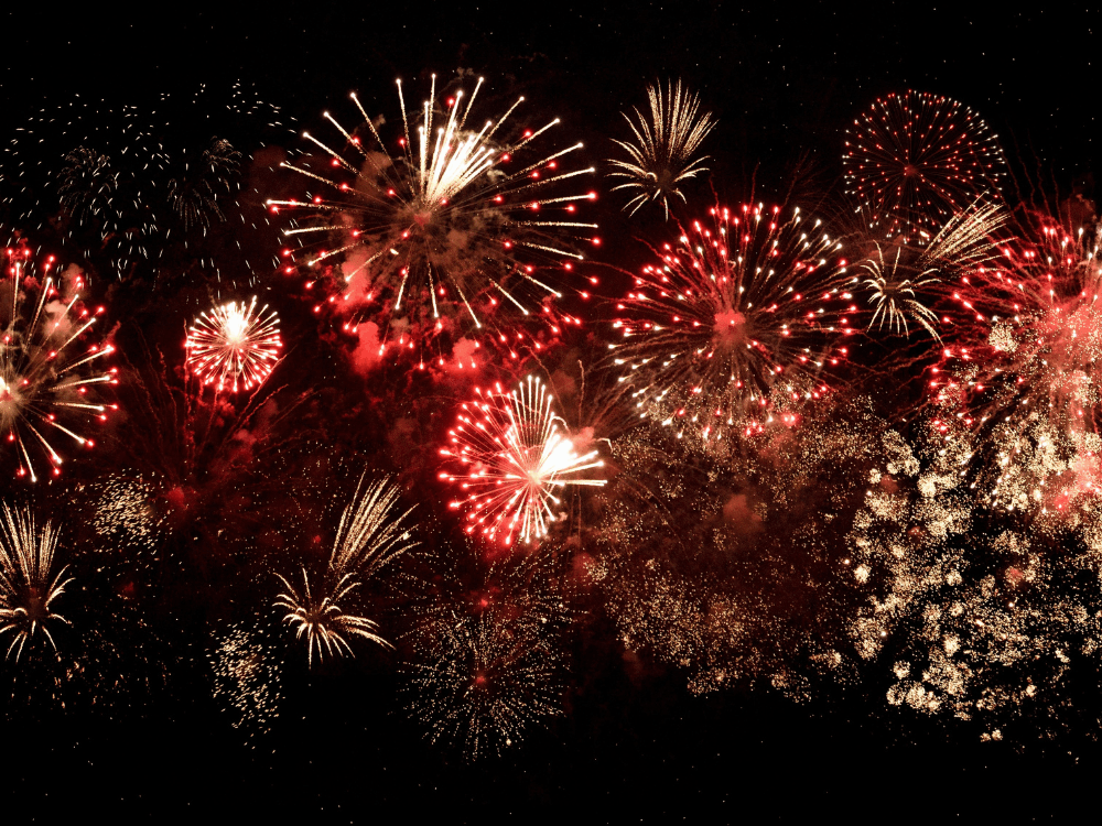 Colorful fireworks explode against a black background, illuminating the night sky with vibrant bursts of light.